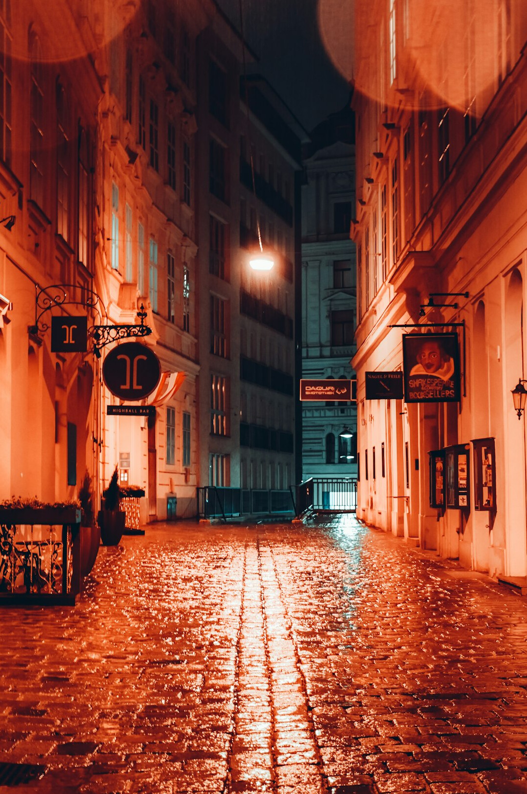 Narrow city street at dusk with warm lights and wet pavement